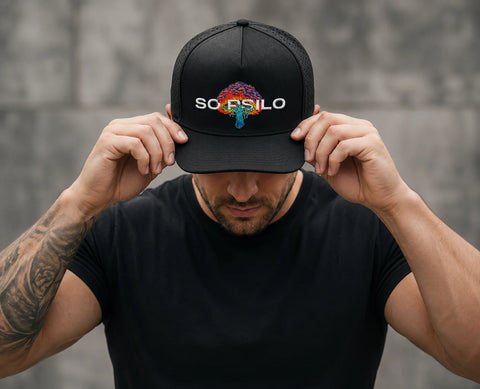 Close-up of a muscular man adjusting a black SOPSILO hat with vibrant mushroom embroidery against an outdoor urban background.